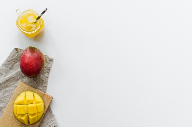Mangue mûre, demi-mangue et un verre de jus de mangue sur une planche à découper en bois.