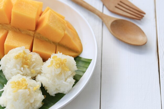 Mangue et riz gluant dans un plat blanc sur un plancher en bois blanc.