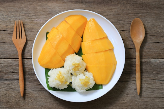 Mangue et riz gluant dans le plat blanc sur plancher en bois.