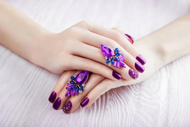 Manicure violette avec des boucles d'oreilles sur fond blanc