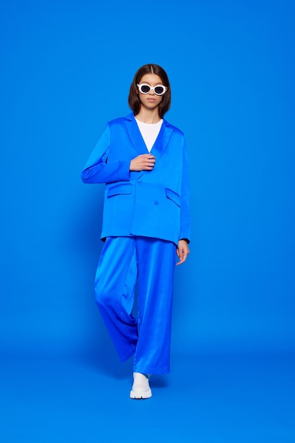 Une mannequin asiatique en costume bleu, bottes blanches et lunettes de soleil.