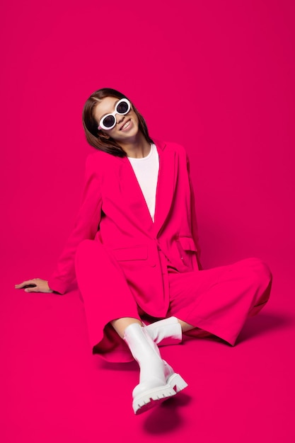 Une mannequin asiatique en costume rose, bottes blanches et lunettes de soleil.