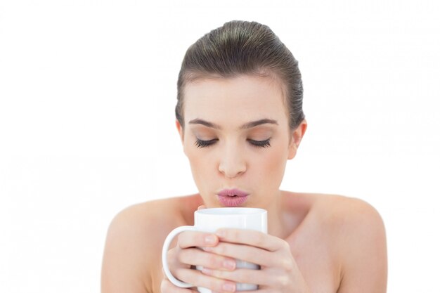 Mannequin aux cheveux bruns naturels paisibles soufflant sur son café