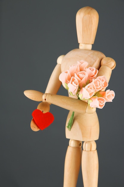 Mannequin en bois tenant le bouquet et le coeur rouge sur le fond gris