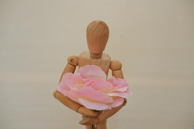 Un mannequin en bois tenant une rose rose sur fond blanc