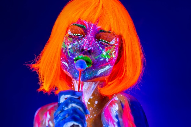 Photo mannequin femme lèche des bonbons sucrés en néon, discothèque. beau modèle fille maquillage lumineux fluorescent coloré