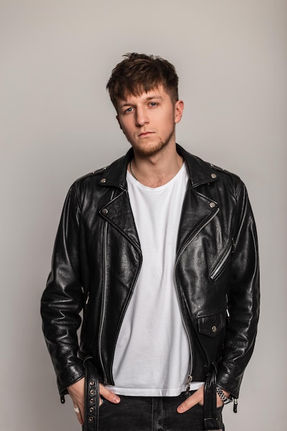 Mannequin jeune homme avec une coiffure à la mode dans des vêtements décontractés avec une veste de rock en cuir noir sur fond gris. Mec élégant à l'intérieur