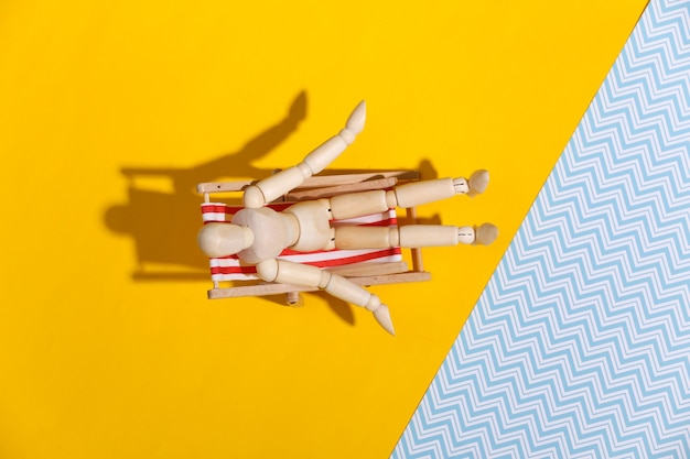 Le mannequin marionnette prend un bain de soleil sur la chaise longue de plage. Studio bleu jaune. Lumière ensoleillée. Concept de vacances à la plage. Repos d'été