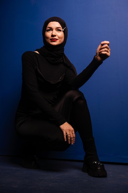 Mannequin musulman en hijab noir pose sur fond bleu en studio. religion islamique.