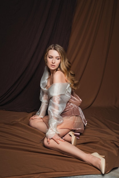 mannequin en robe transparente assise sur le sol, femme blonde romantique dans un studio