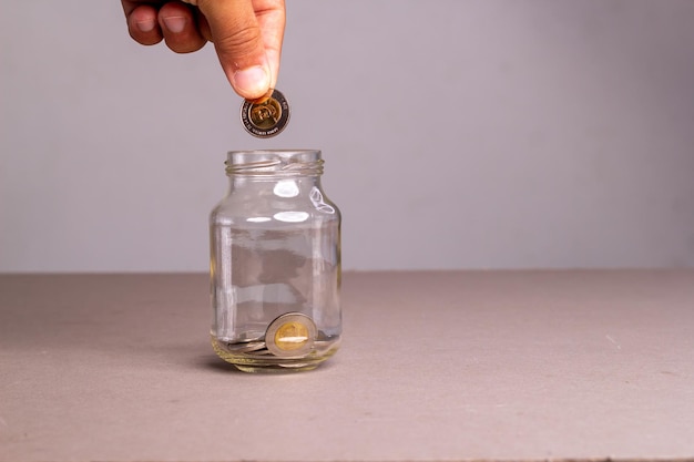 Mano pone dinero en monedas dominicanas en un frasco de vidrio "ahorros".