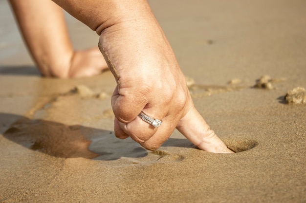 Mano De Una Mujer Con Anillo Escribiendo Un Mensaje Sobre La Arena Mojada De La Playa En Verano