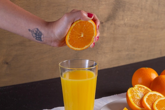 Mano de una mujer exprime el zumo de naranja en un vaso sobre una mesa, fondo de fruta de naranja