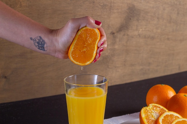 Mano de una mujer exprime el zumo de naranja en un vaso sobre una mesa, fondo de fruta de naranja