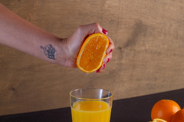 Mano de una mujer exprime el zumo de naranja en un vaso sobre una mesa, fondo de fruta de naranja