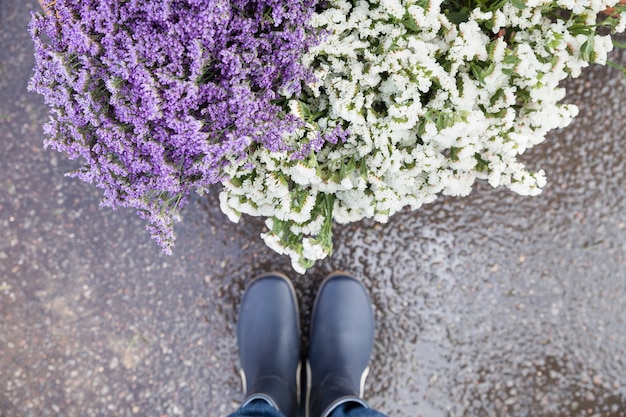 Mans jambes en bottes en caoutchouc bleu debout près d'un panier avec de belles fleurs de jardin après la pluie