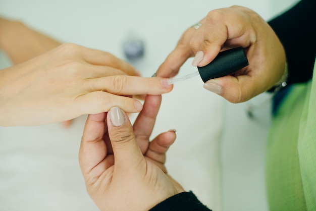 Manucure appliquant un adoucissant pour cuticules ou un vernis à ongles transparent sur les ongles d'une cliente dans un spa ou un salon de beauté en gros plan sur leurs mains