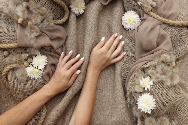 Manucure beige clair avec chrysanthèmes sur toile de jute.