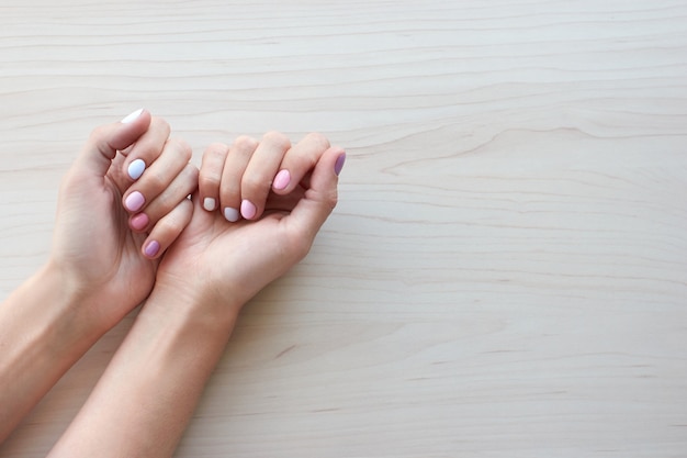 Manucure élégante à la mode féminine en blanc, rose et bleu pastel. Les mains de la belle jeune femme sur fond en bois. Copiez la bannière de l'espace.