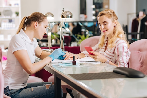 Manucure féminine attrayante enlever la cuticule et la femme à l'aide de téléphone