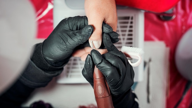 Manucure féminine polissant les ongles à la main d'un homme latino avec perceuse à ongles vue d'en haut gros plan