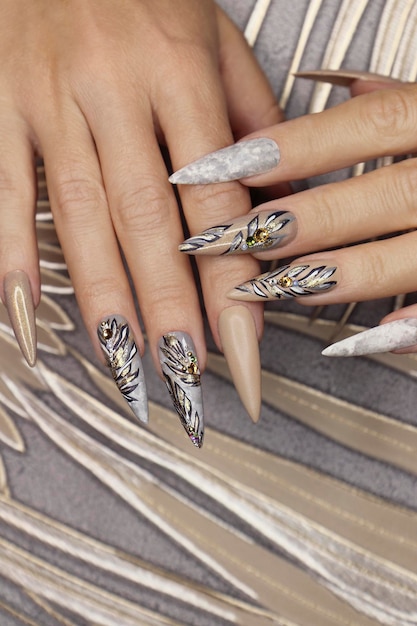 Manucure sur la forme pointue des ongles avec un motif de feuilles avec des strass