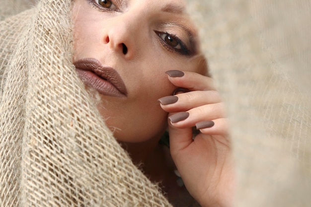 Manucure et maquillage mat chocolat sur une femme avec un décor en toile de jute.