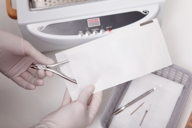 Manucure méconnaissable mettant des pinces à ongles dans une enveloppe en papier pour la stérilisation à la chaleur sèche