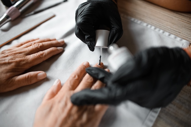 Manucure peint des ongles à un client âgé, gros plan. Salon de beauté