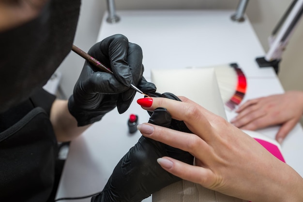 Le manucure peint les ongles du client avec du vernis rouge Concept de soin des ongles