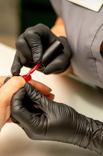 Manucure professionnelle Une manucure peint les ongles féminins d'un client avec du vernis à ongles rouge dans un salon de beauté en gros plan Concept de l'industrie de la beauté