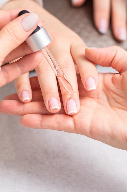 Manucure professionnelle verser de l'huile sur les ongles manucure française de femme dans un salon de beauté.