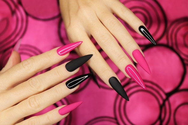 Manucure rose et noire à la mode sur de longs ongles pointus