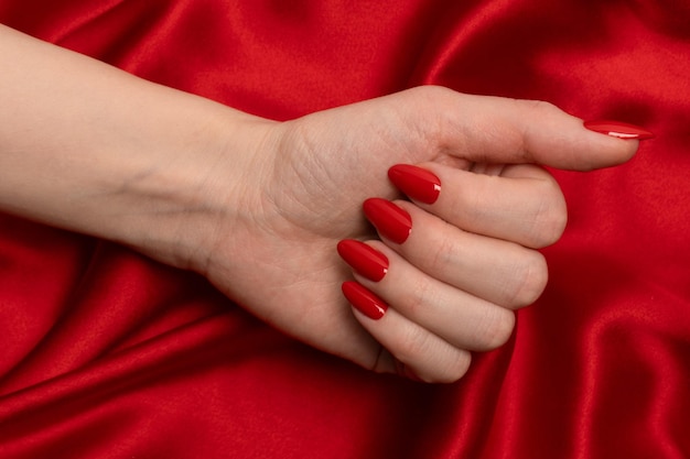 Manucure rouge sur les mains d'une femme sur un fond de soie rouge de luxe