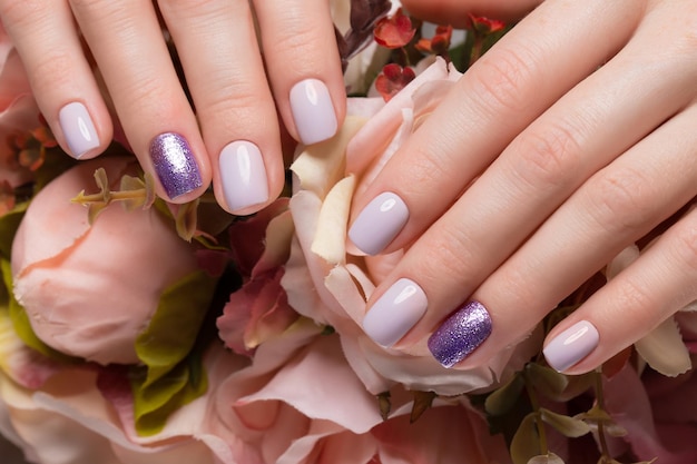 Manucure soignée violette sur les mains féminines sur fond de fleurs. Conception d'ongles