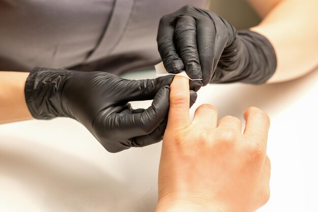 Le manucure termine la procédure de polissage et de nettoyage des ongles rouges avec un tampon de serviette en coton dans un salon de beauté en gros plan