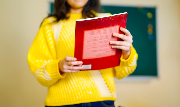 Manuel rouge dans les mains sur la vue de face Fille en pull jaune sur fond flou