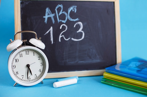 Manuels et réveil avec tableau d'école sur fond bleu