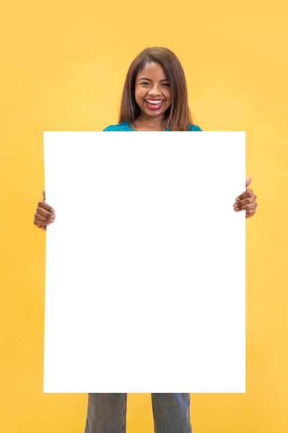 Maquette d'affiche - Fille tenant une bannière blanche vierge avec espace de copie sur un fond de studio jaune