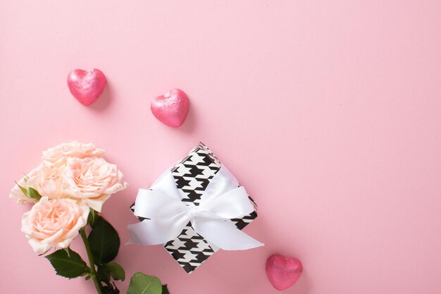 Une maquette d'une bannière de la Saint-Valentin avec une boîte-cadeau de bonbons en forme de coeur et un bouquet de roses sur fond rose