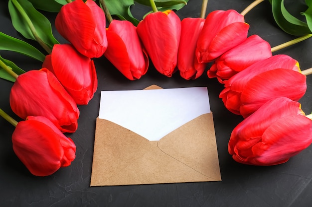 Maquette de bouquet de tulipes rouges fraîches et carte de voeux vierge dans une enveloppe kraft