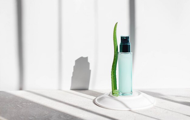 Maquette de bouteille en verre vert avec des feuilles d'aloe vera sur fond clair. Cosmétiques naturels et biologiques. Concept de soins de la peau pour les femmes, photo pour les réseaux sociaux avec espace copie.