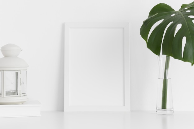 Maquette de cadre blanc avec accessoires d'espace de travail et une feuille de monstère dans un vase sur une table blancheOrientation portrait