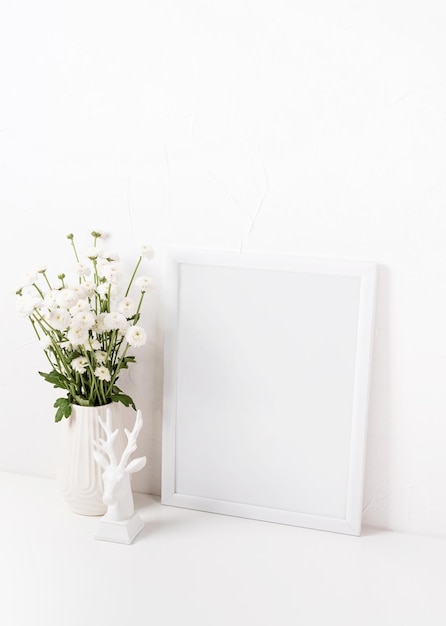 Maquette de cadre blanc avec des fleurs de chrysanthème dans un vase sur un tableau blanc