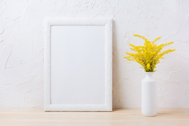 Maquette de cadre blanc avec de l'herbe à fleurs jaunes ornementales dans un vase