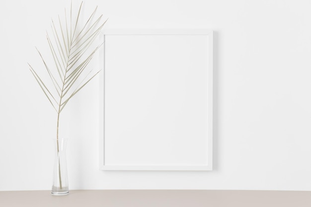 Maquette de cadre blanc sur le mur avec une feuille de palmier