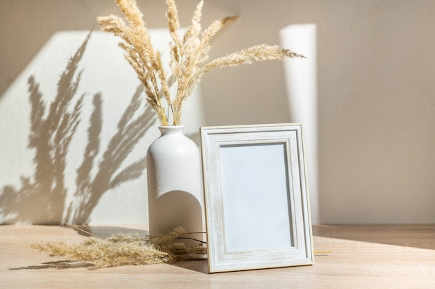 Maquette de cadre photo blanc portrait sur table en bois Vase en céramique moderne avec fleurs séchées