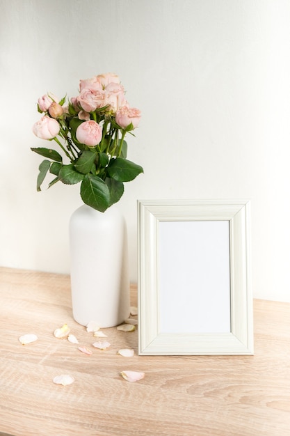 Maquette de cadre photo blanc portrait sur table en bois vase en céramique moderne avec des roses fond de mur blanc intérieur scandinave