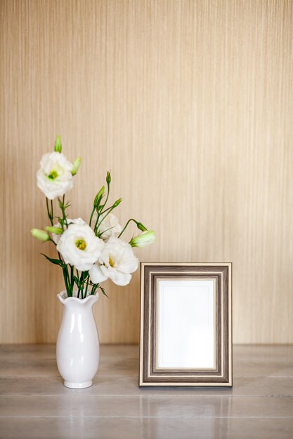 Maquette avec cadre photo, fleurs blanches Eustoma ou Lisianthus dans un vase sur une table en bois avec espace de copie.