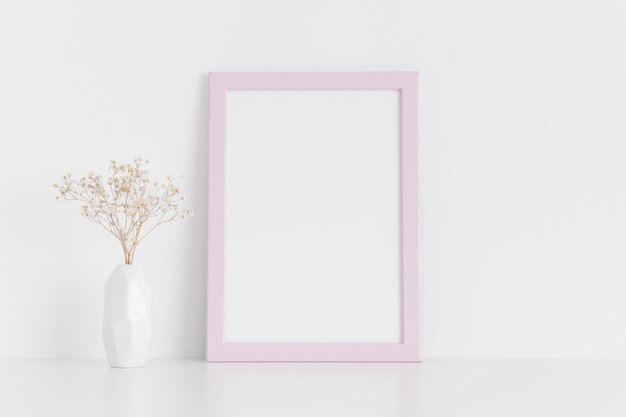 Maquette de cadre rose avec une gypsophile dans un vase sur une table blancheOrientation portrait